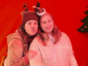 In der Fotobox. Roter Hintergrund. Zwei Menschen mit lustigen Weihnachtshütchen die Grimassen ziehen.