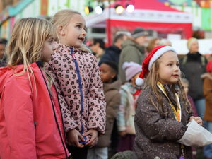 3 staunende Mädchen im Vordergrund. Das Mädchen rechts trägt eine rote Weihnachtsmütze. Im Hintergrund weitere Gäste.