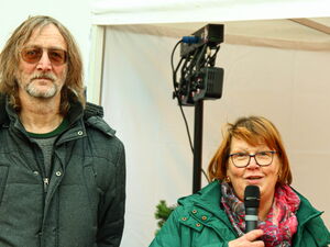 Mann und Frau stehen in einem Pavillon. Frau spricht in ein Mikrofon.