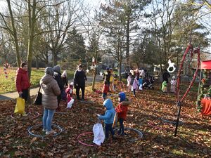 Draußen, Wiese mit Laub, Bäume. Wintersonne scheint. Hula Hoop Reifen liegen auf der Erde, einige Kinder, Jugendliche stehen in diesen. Weihnachtlich geschmückter Markt.