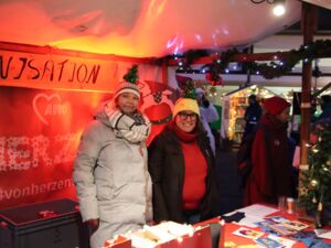 Zwei Frauen, lächeln in die Kamera. Sie stehen in einem roten, weihnachtlich geschmückten Pavillon.