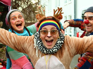 2 Clowns haben ein fröhliches wildes Rentier in ihrer Mitte das breit grinst. Frau im Reintier-Kostüm.