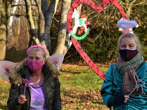 Als Fee verkleideten Frau. Die Frau hat Feenflügel, eine pinke Maske und trägt ein blasrosa-lila Kleid unter einer dunkelgrünen Winterjacke. Daneben Frau mit Engel Heiligenschein Winterkleidung mit Maske. Dahinter ein mit Lichterketteumwickeltes Herz.